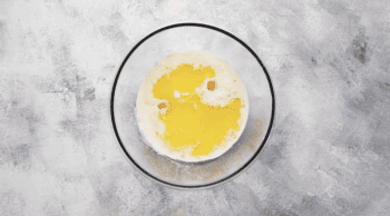 A blueberry pancake recipe with an egg in a glass bowl on a gray background.