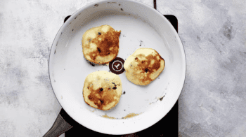 Two blueberry pancakes in a pan on a stove top.