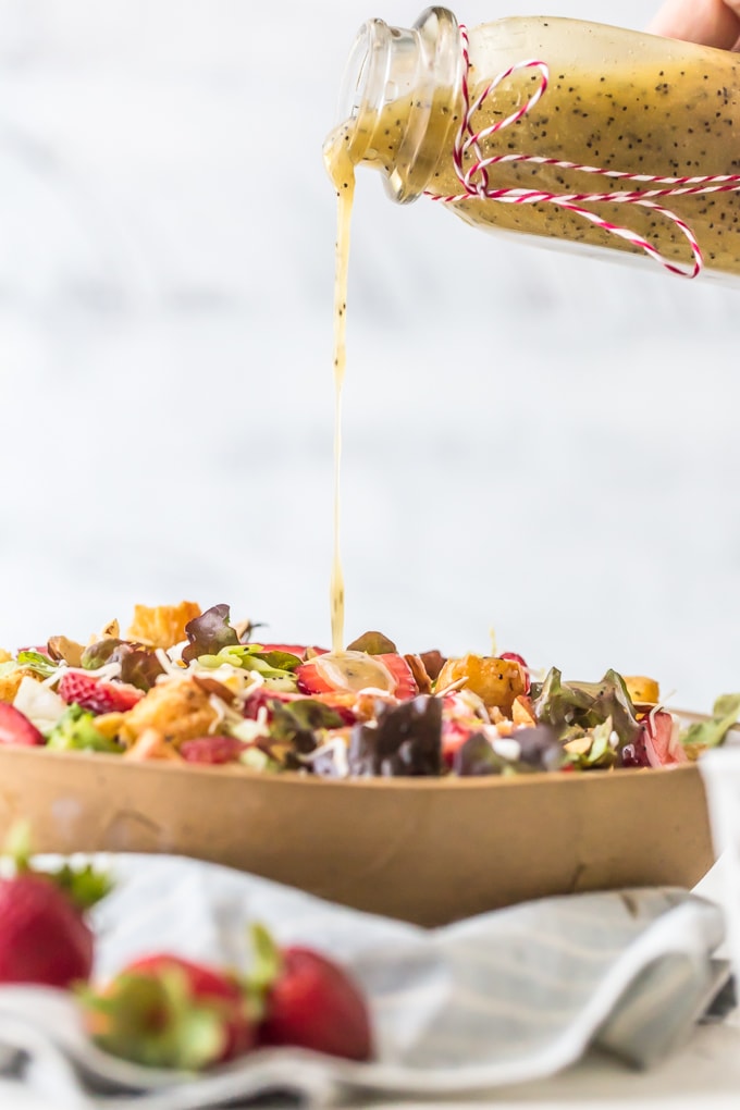 Pouring poppyseed dressing over a strawberry poppyseed salad