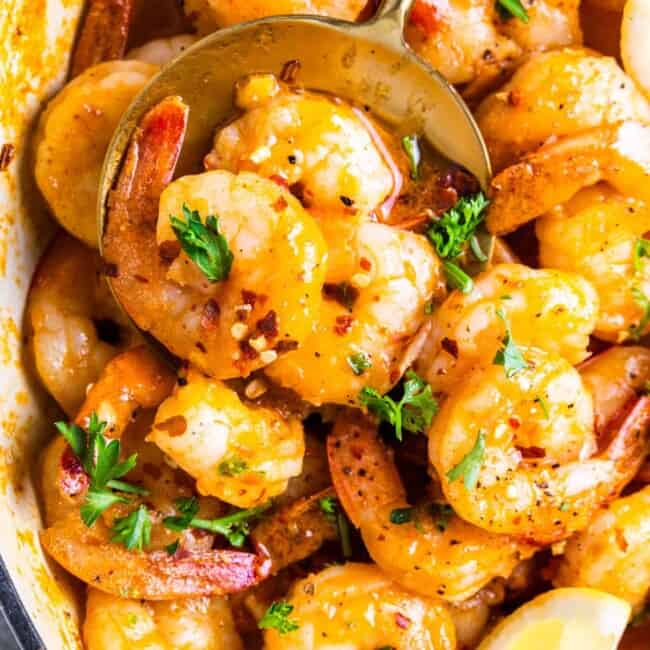 partial close-up view of garlic butter shrimp in a white pan with a spoon.