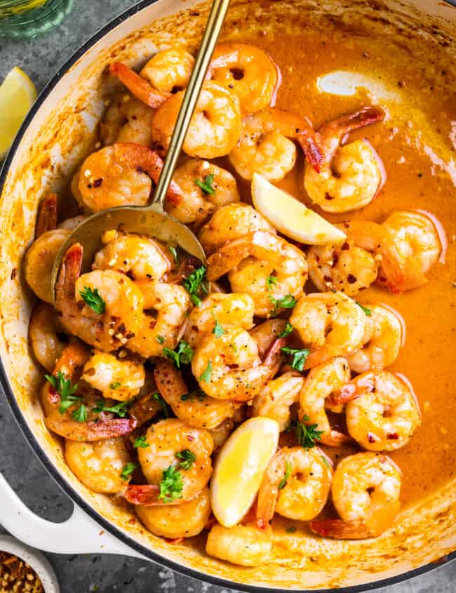 overhead view of garlic butter shrimp in a white pan with a spoon and lemon wedges.