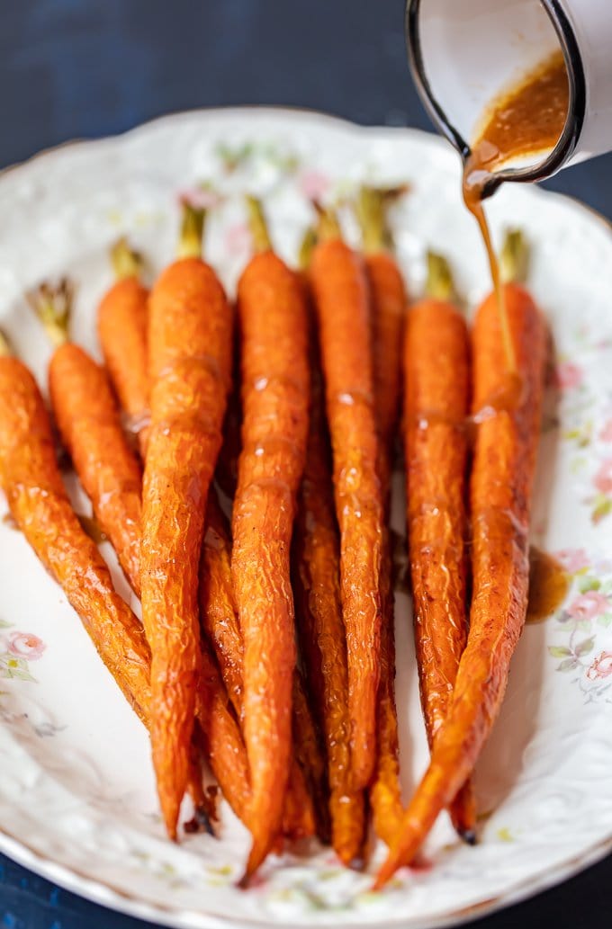 Pouring honey glaze over ginger carrots on a serving platter