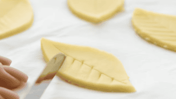 using a knife to imprint designs on a pastry dough leaf.