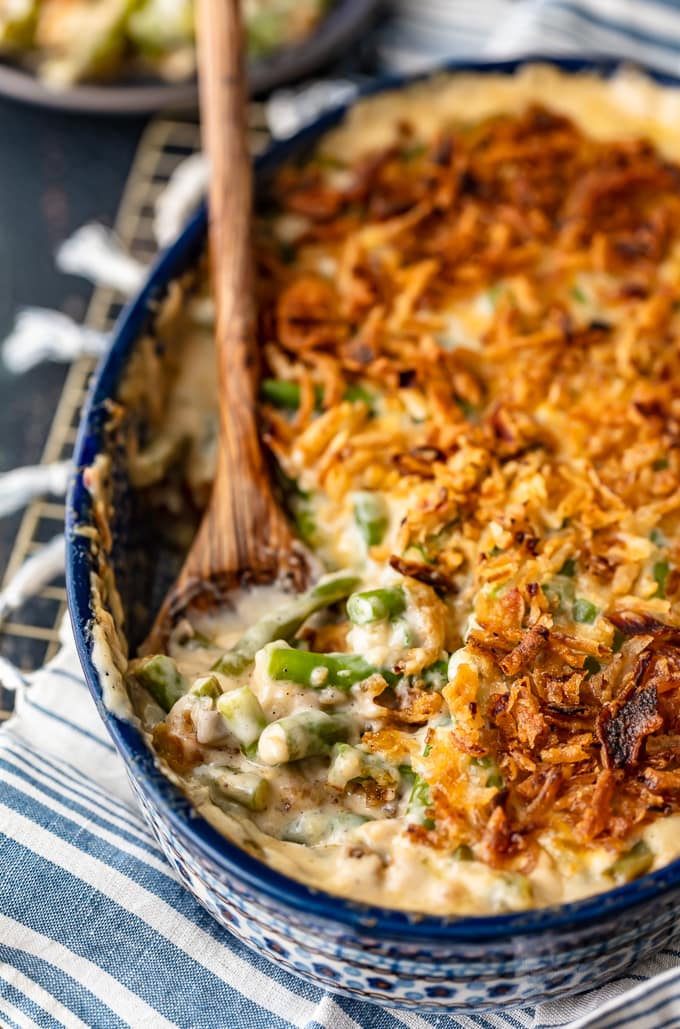 Cheesy classic green bean casserole in a blue dish with a wooden spoon.