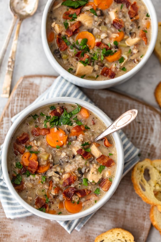 Two bowls of creamy chicken and rice soup topped with bacon, carrots, and thyme