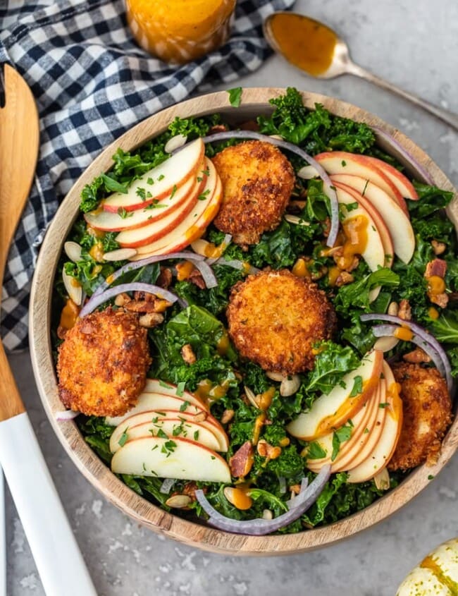 This Autumn Kale Salad recipe is the salad of the season! Made with kale, apples, onions, pumpkin seeds, bacon, fried goat cheese and a maple pumpkin salad dressing, it is the perfect fall salad idea. This delicious kale apple salad makes a tasty and healthy meal you'll want to eat all season long!