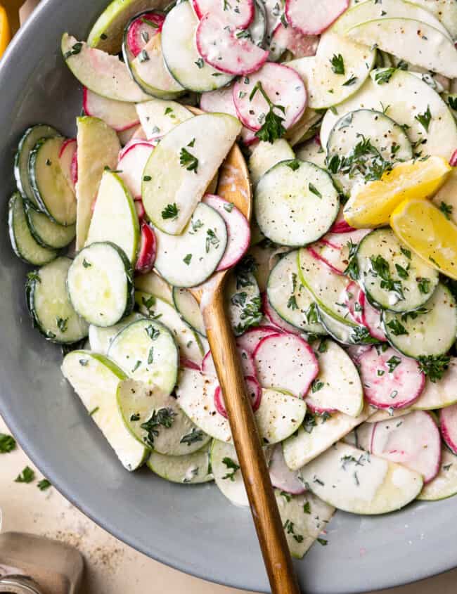 creamy cucumber salad in a gray serving bowl with wooden salad serving utensils.