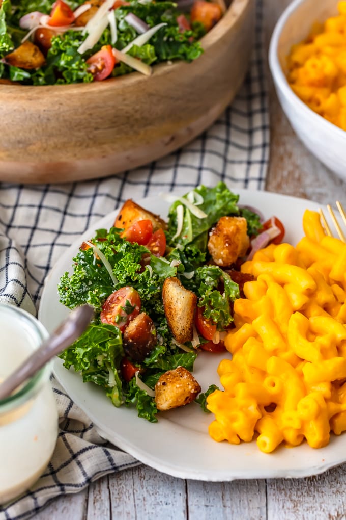 A white plate with mac and cheese and a kale caesar salad