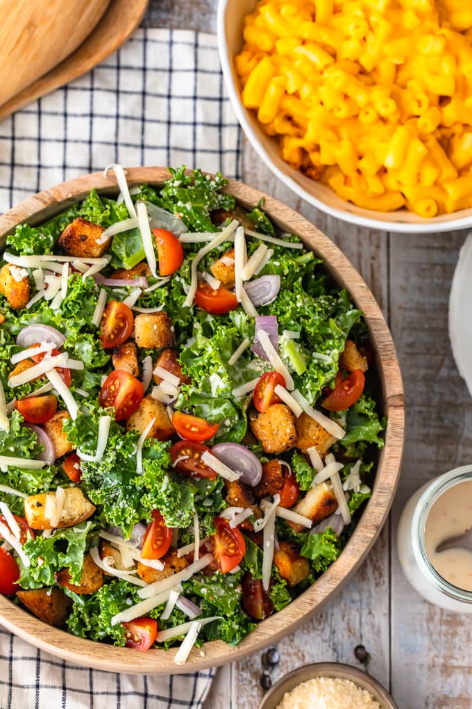 Kale Caesar Salad with tomatoes, shallots, cheese, and homemade croutons next to a bowl of macaroni and cheese