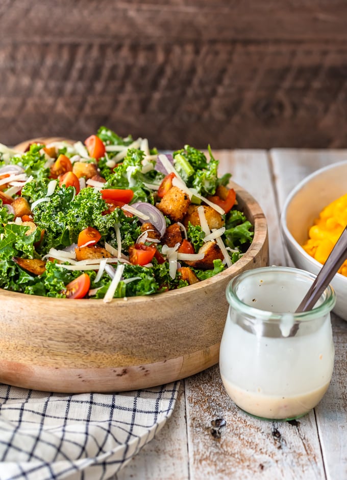 Serving bowl of kale caesar salad next to a jar of homemade caesar salad dressing