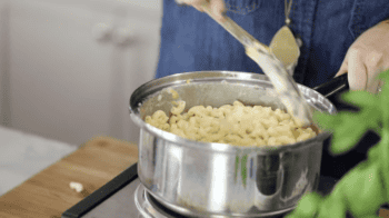 stirring mac and cheese in a pot with a wooden spoon.