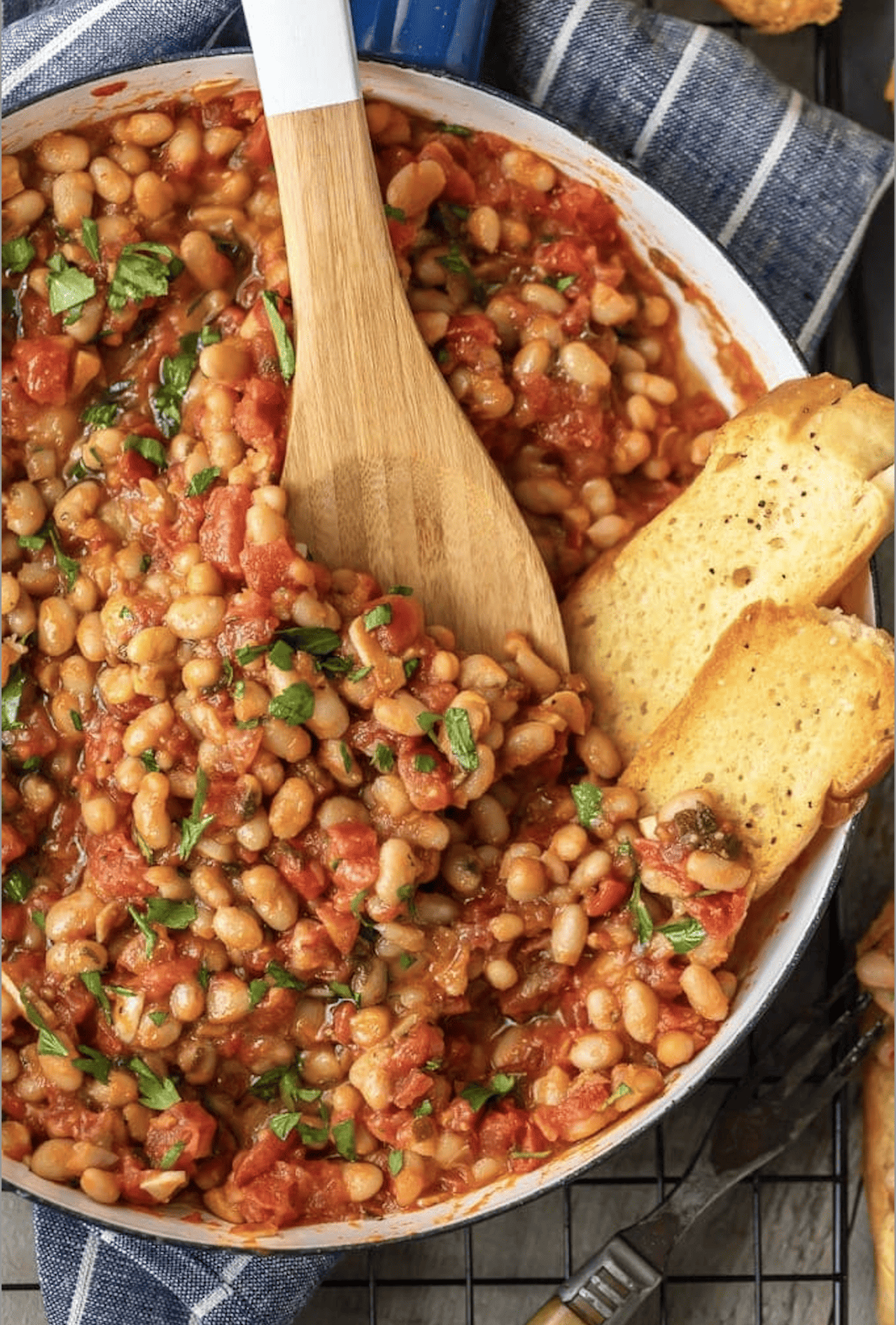 A pan full of white beans in tomato sauce, being stirred with a wooden spoon.