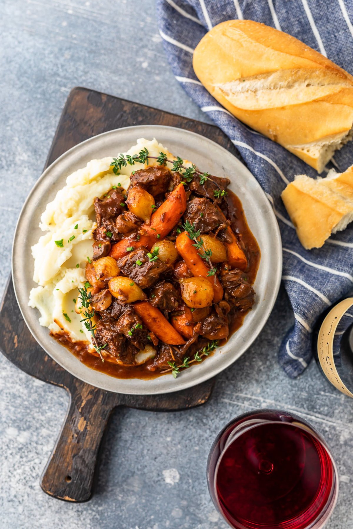 overhead view of beef burgundy next to a loaf of bread on a striped dish towel