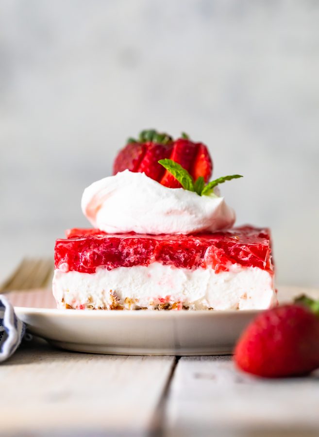 a slice of strawberry pretzel salad on a plate, topped with whipped cream and fresh berries.