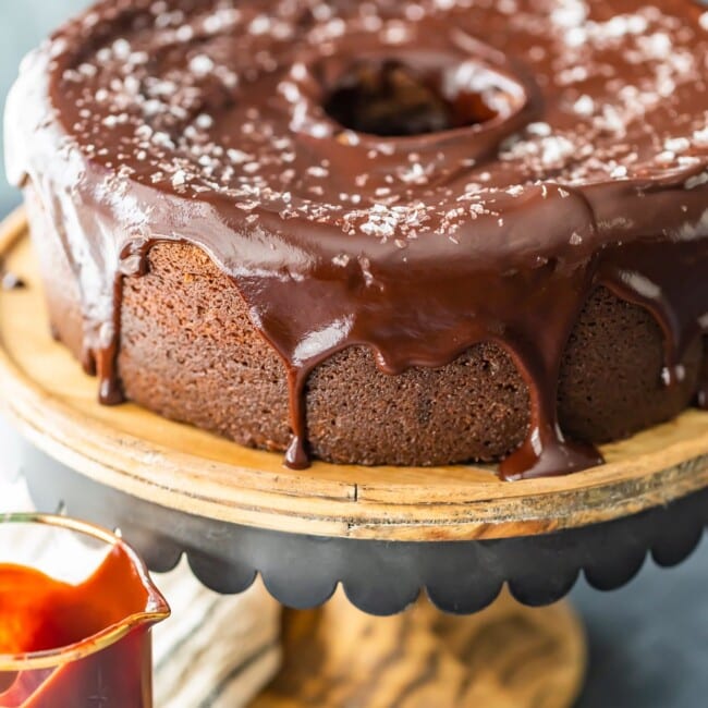 a decadent chocolate bundt cake with luscious chocolate ganache icing is displayed on a rustic wooden plate.