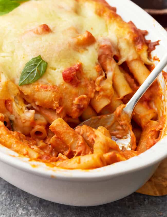 close up of baked ziti in a baking dish with a spoon.