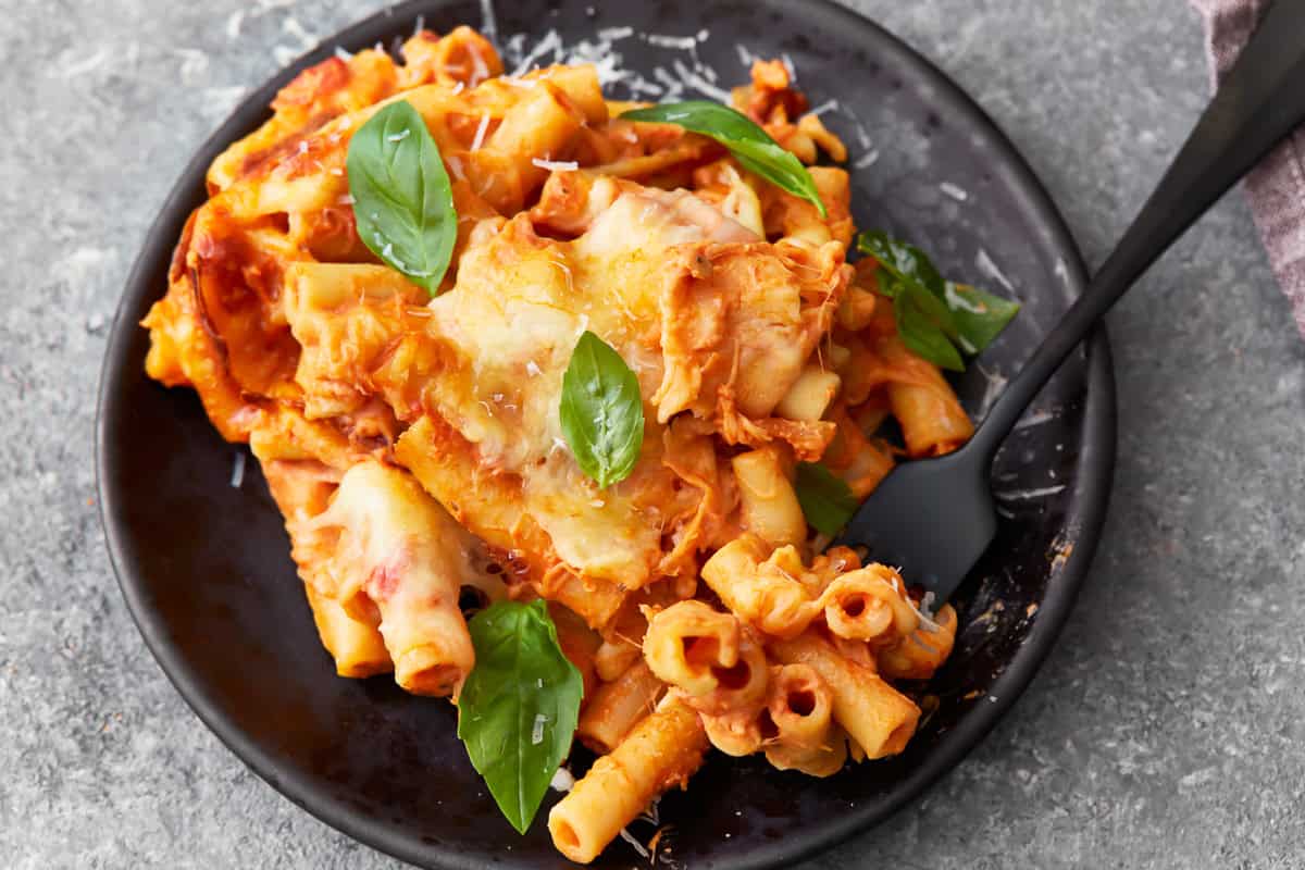 a serving of baked ziti on a black plate with a fork.