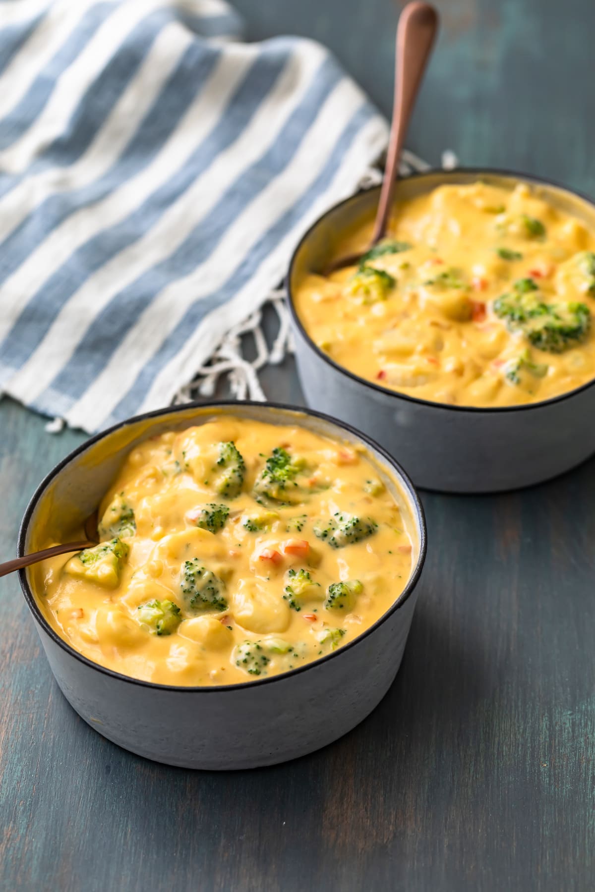 two bowls of broccoli cheese gnocchi soup, next to a striped dish towel