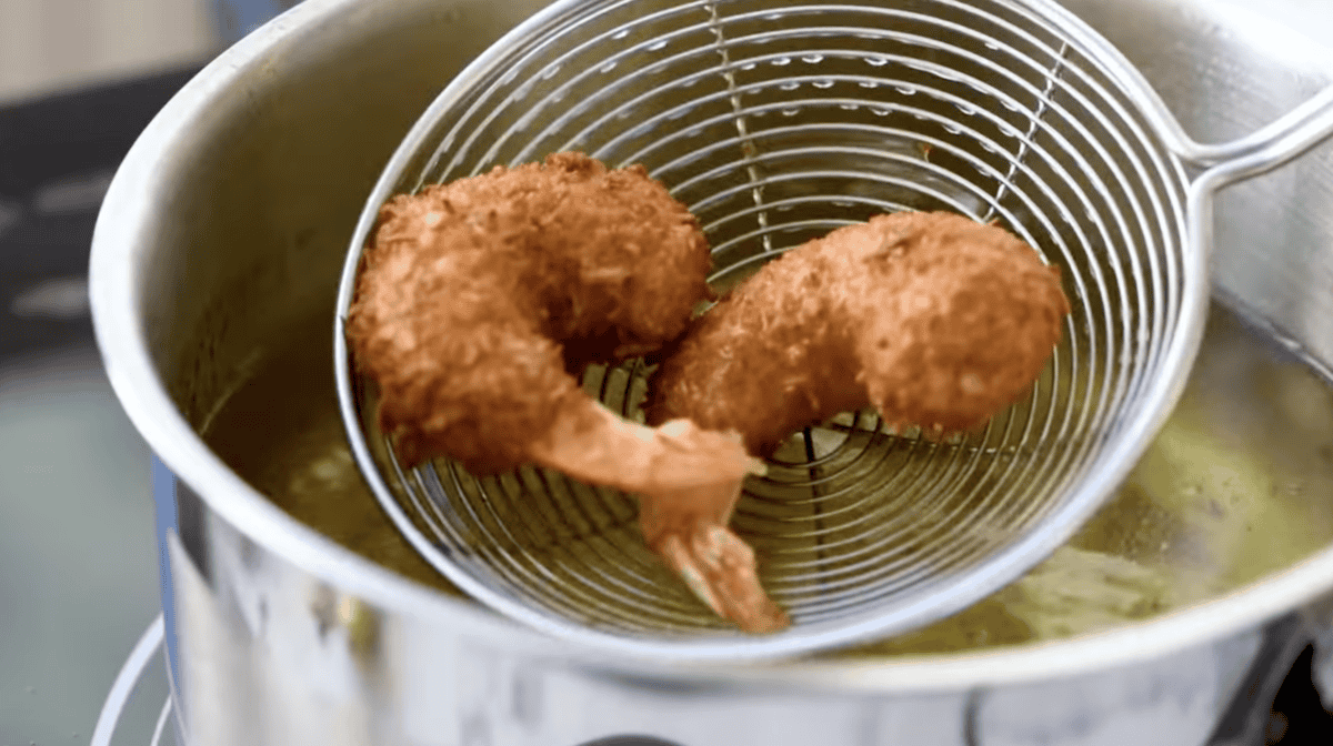 2 fried coconut shrimp in a spider strainer.