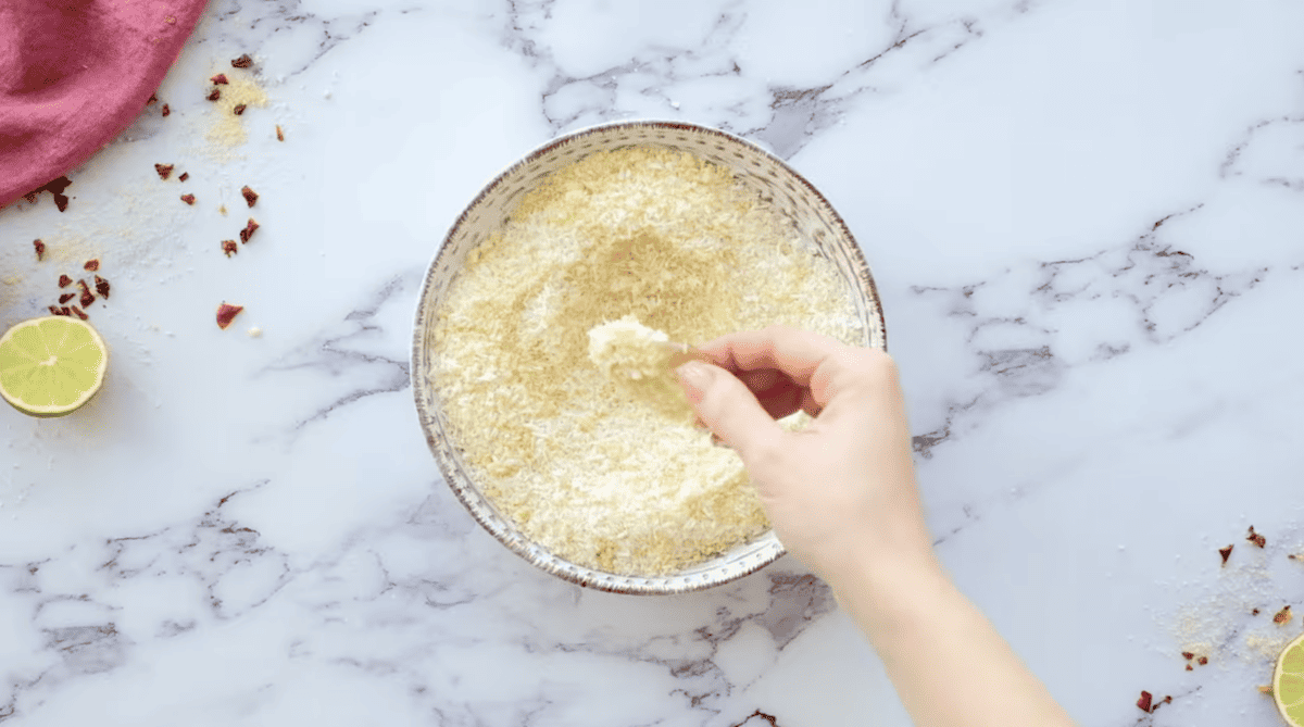 a dredged shrimp over a bowl of breadcrumbs.