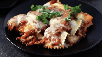 A plate of lasagna with meat, cheese, and pasta on a black plate.