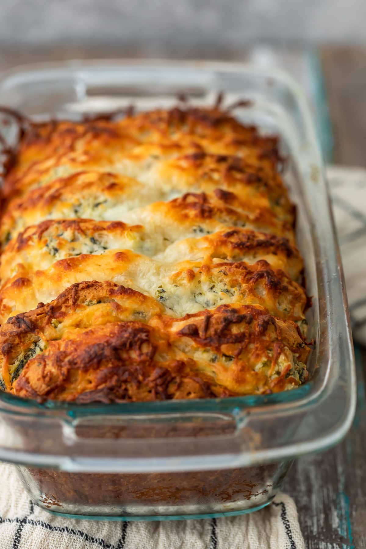 loaf of pull apart bread in a bread pan, topped with cheese and parsley butter