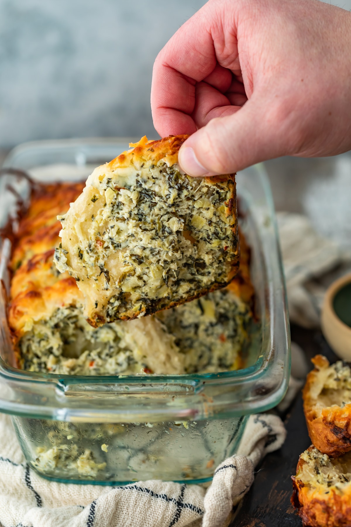 hand pulling a piece of spinach artichoke bread out of a glass dish