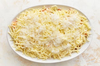 layered baked ziti in an oval baking dish topped with cheese.