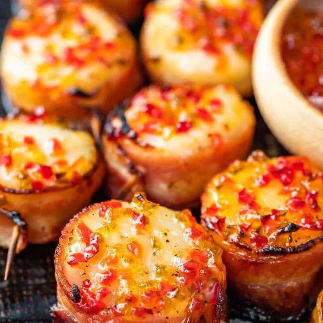 Bacon-wrapped scallops served on a wooden board.