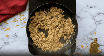 A sausage and potato casserole cooking in a frying pan on a marble countertop.