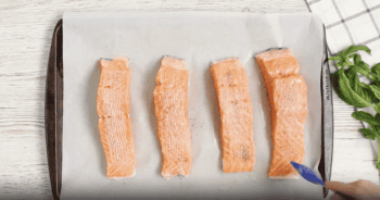 4 salmon filets on a baking sheet topped with a creamy sauce.