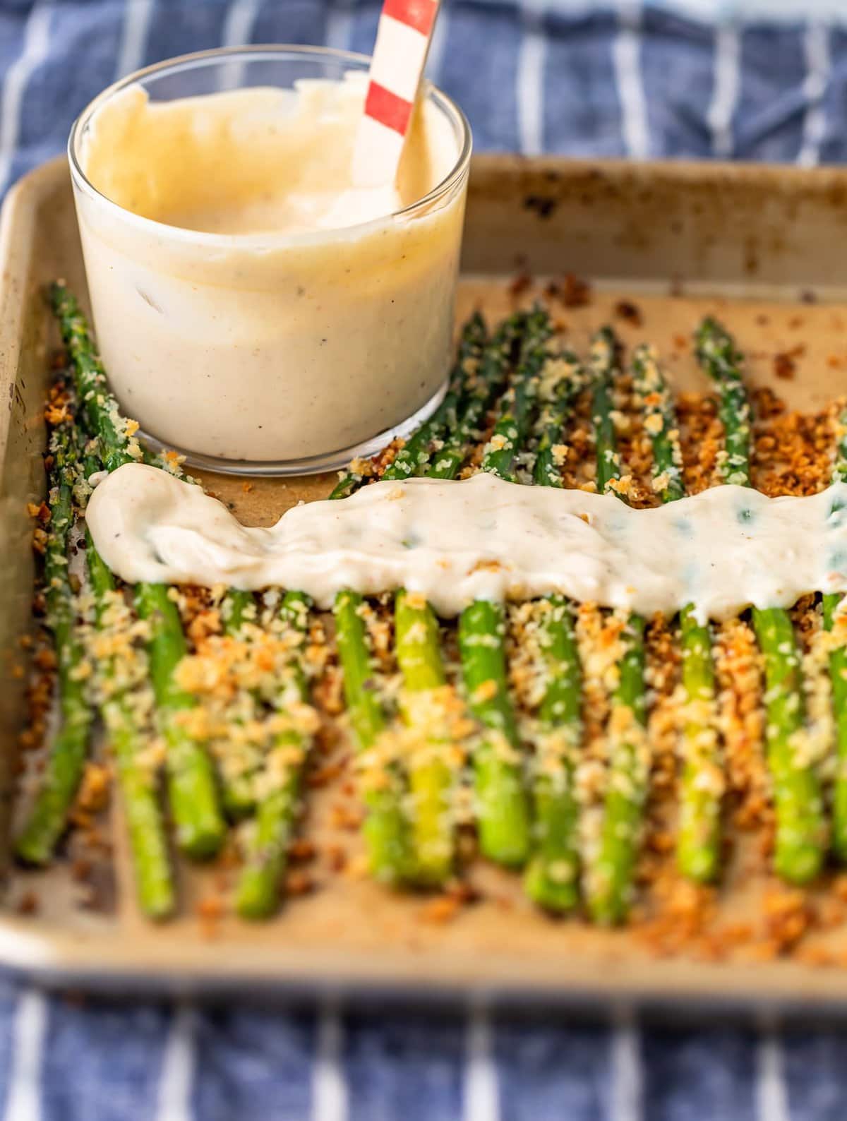 a baking sheet with asparagus and a bowl of aioli