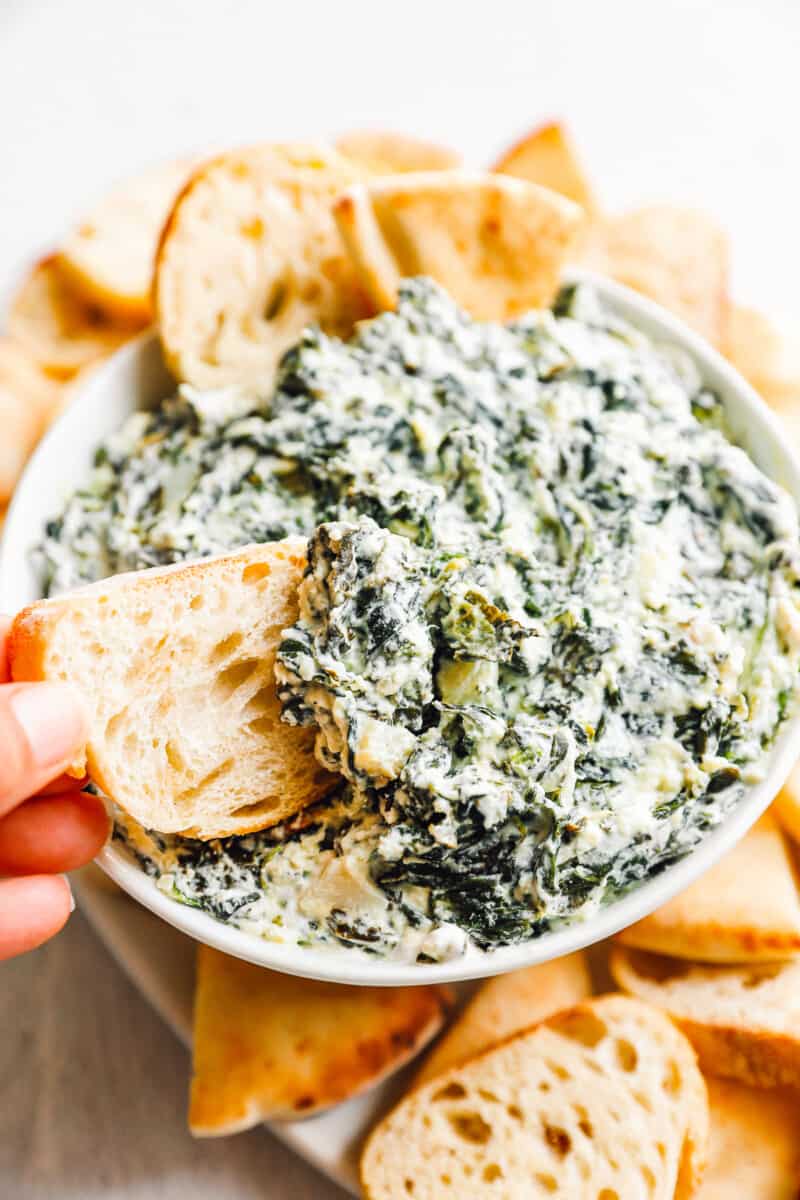 crockpot spinach dip in a white bowl with dippers