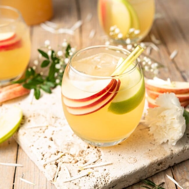 An apple pie drink in a round glass with slices of apple and a straw