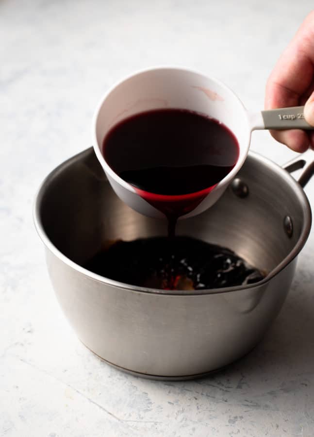 a person pouring red wine onto a sizzling new york strip steak in a pan.