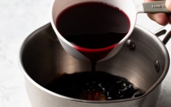 a person pouring red wine onto a sizzling new york strip steak in a pan.