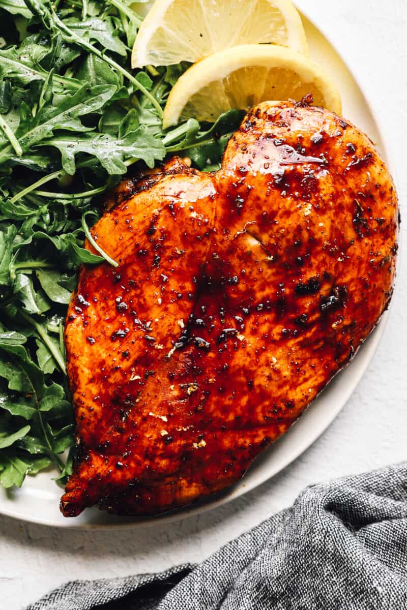 up close balsamic chicken on white plate with simple salad and lemon