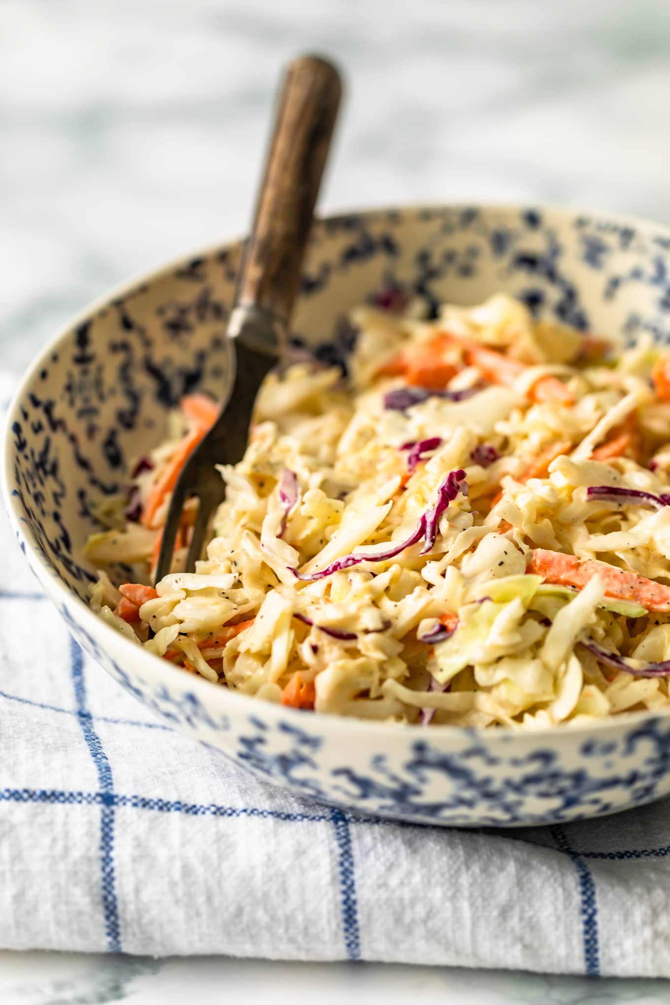 Closeup view of coleslaw in a white and blue bowl with a fork.