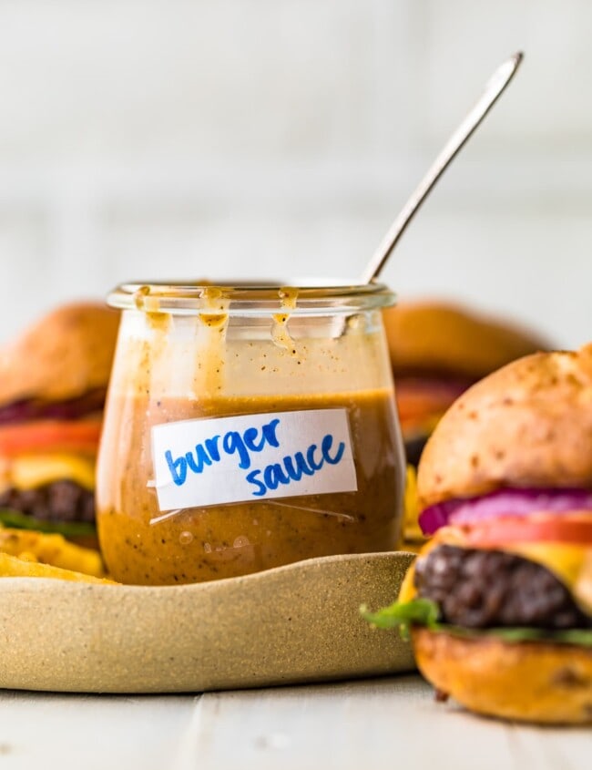 burger sauce in a cup with a spoon and burgers beside it