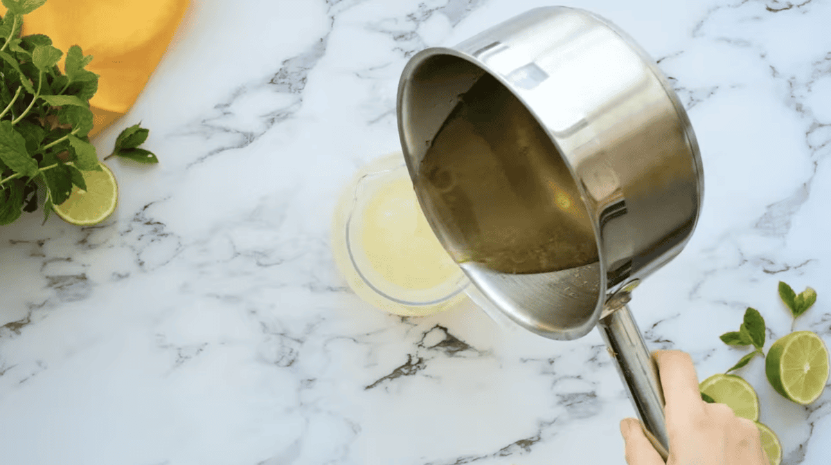 pouring lime simple syrup into a pitcher of limeade.