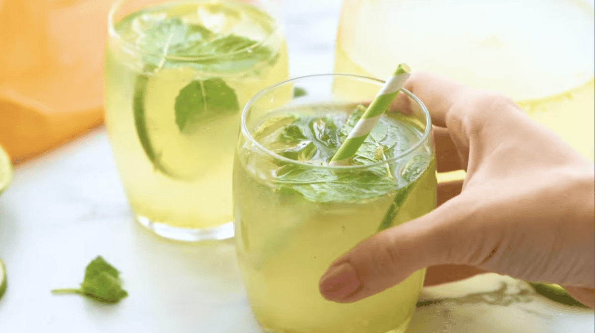 holding a glass of limeade with ice, mint, lime slices, and a straw.