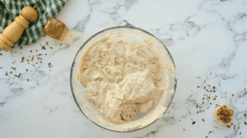 chicken thighs coated in seasoned yogurt in a glass bowl.