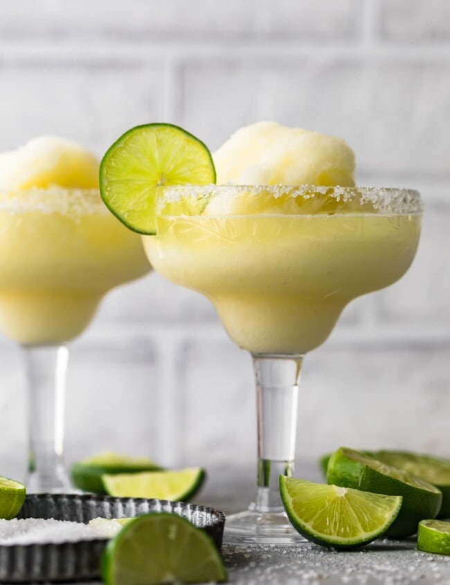 two frozen margarita glasses surrounded by sliced limes