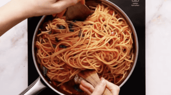 A person is stirring pasta pomodoro in a pan.