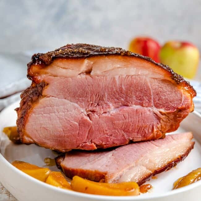 A side shot of a glazed ham with cooked apples