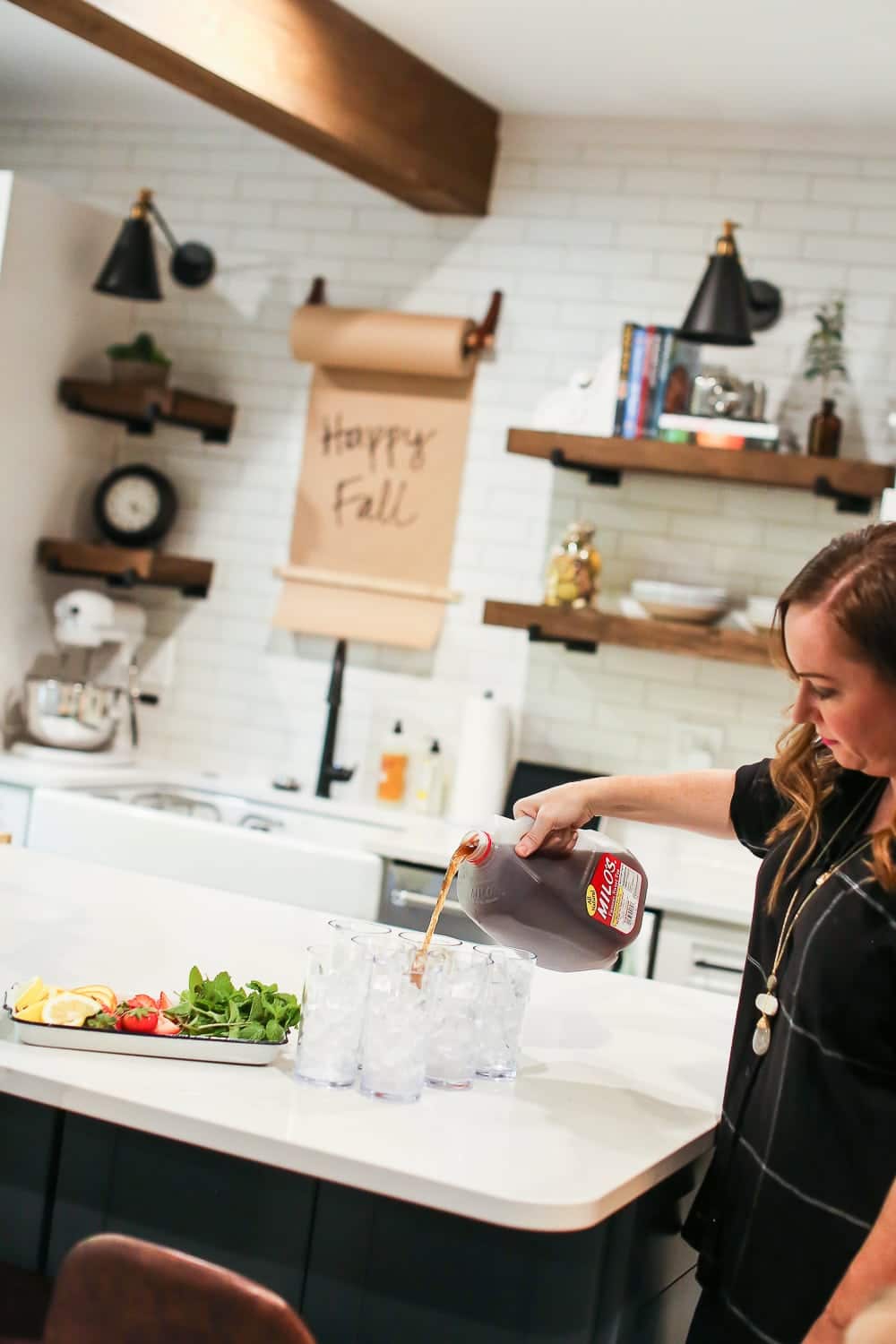 A women pouring Milo's Sweet Tea into glasses filled with ice inside of a kitchen