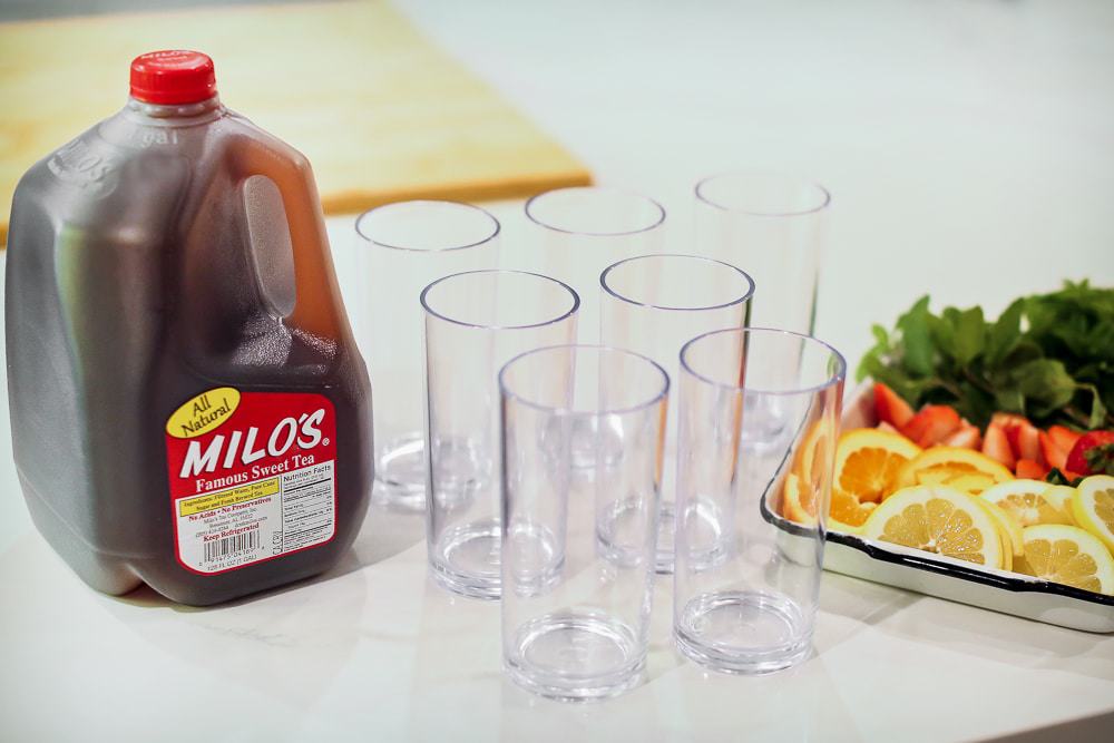 A gallon of Milo's Sweet Tea and glasses sitting on a table