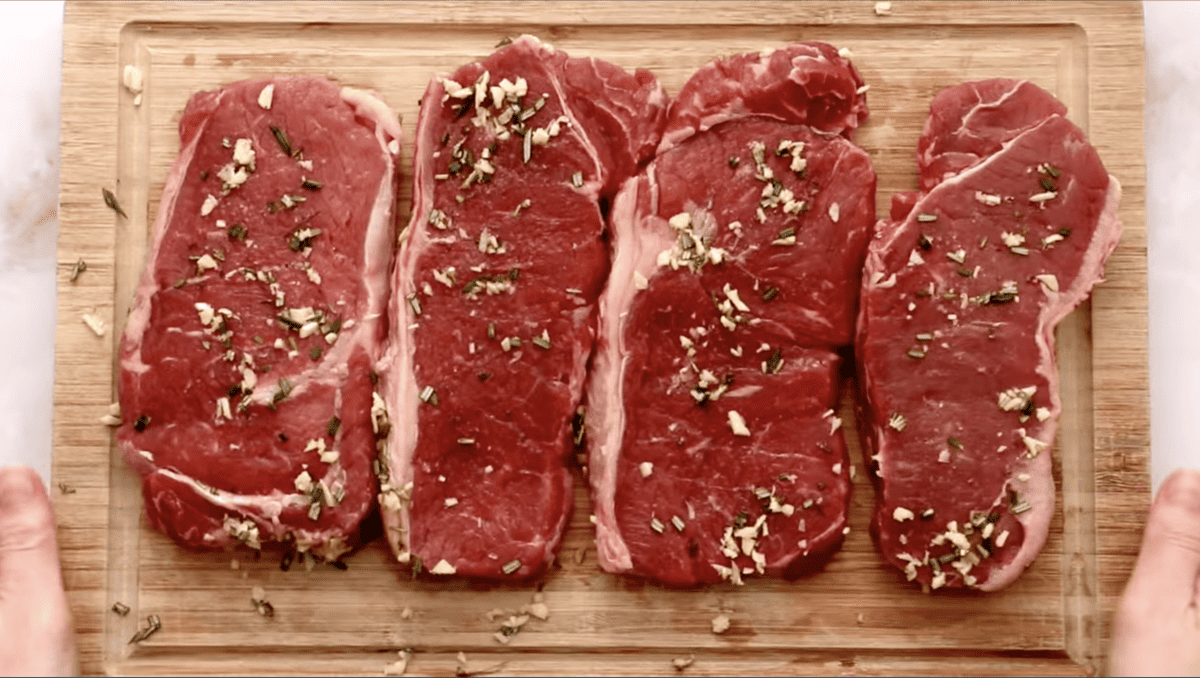 Four pieces of rosemary steak on a cutting board.