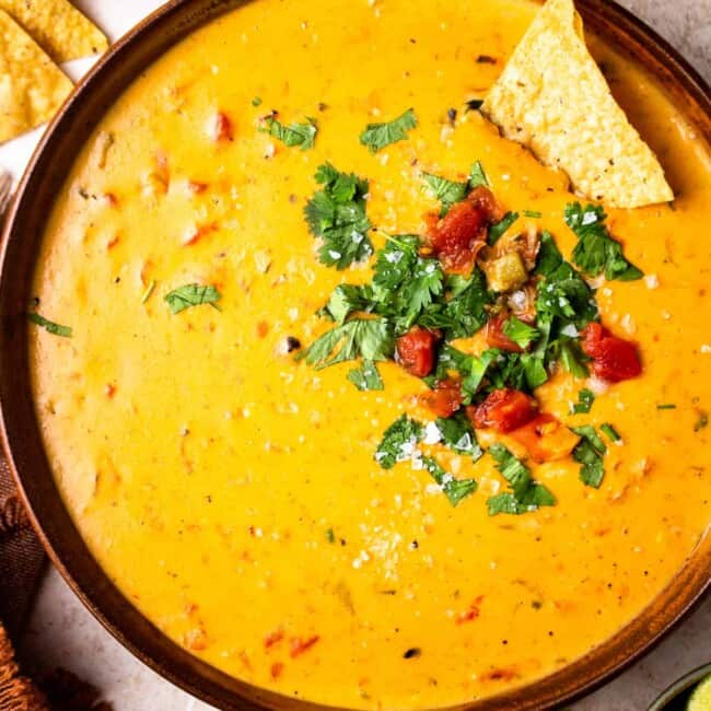 bowl of crockpot queso garnished with tomatoes and cilantro with tortilla chips