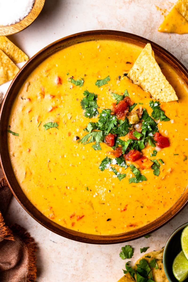 bowl of crockpot queso garnished with tomatoes and cilantro with tortilla chips